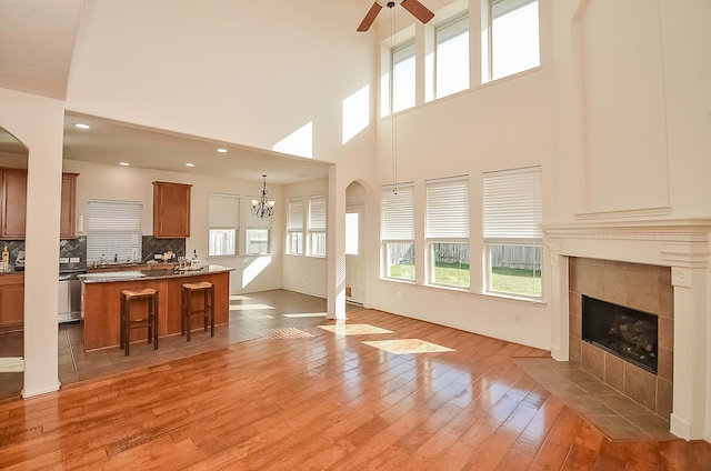 unfurnished living room featuring ceiling fan with notable chandelier, a tiled fireplace, a towering ceiling, and light hardwood / wood-style flooring