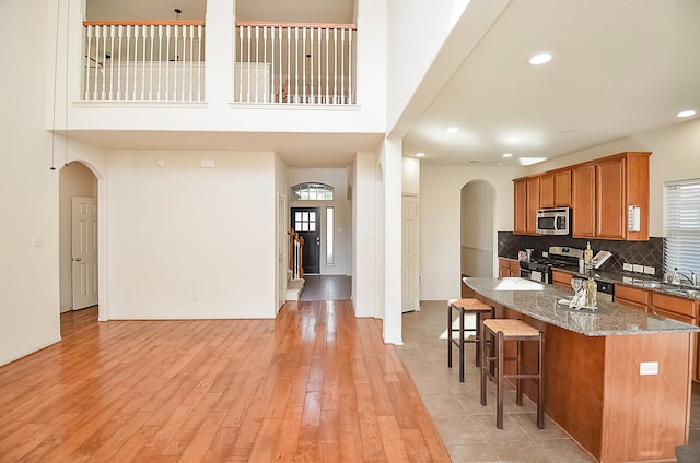 kitchen featuring light wood-type flooring, decorative backsplash, stainless steel appliances, a breakfast bar area, and stone counters