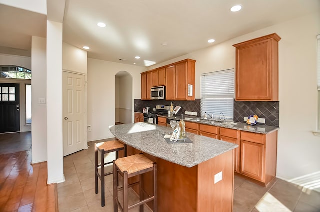 kitchen featuring light stone counters, tasteful backsplash, appliances with stainless steel finishes, a center island, and light hardwood / wood-style floors