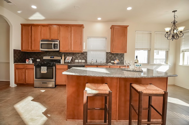 kitchen featuring an inviting chandelier, sink, light stone countertops, appliances with stainless steel finishes, and a kitchen bar