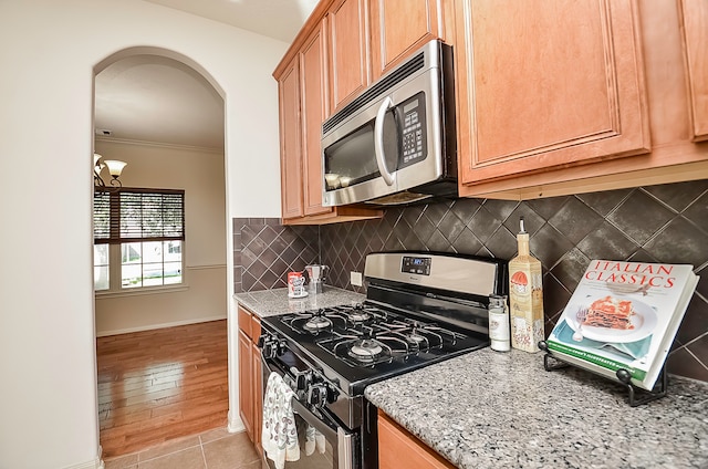 kitchen with light hardwood / wood-style flooring, decorative backsplash, light stone countertops, ornamental molding, and appliances with stainless steel finishes