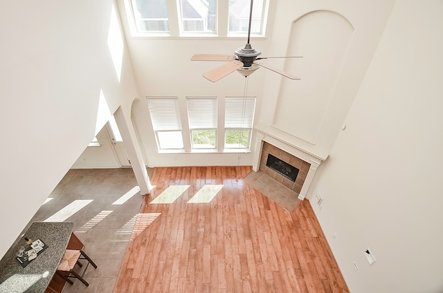 unfurnished living room featuring a fireplace, light hardwood / wood-style floors, a high ceiling, and ceiling fan