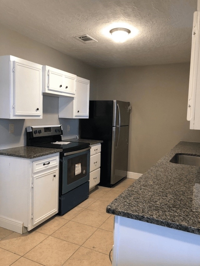 kitchen featuring a textured ceiling, stainless steel refrigerator, white cabinetry, and electric range