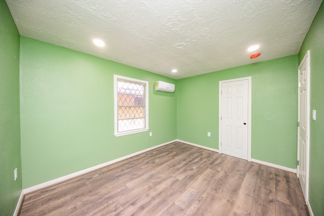 empty room with a textured ceiling, hardwood / wood-style floors, and a wall mounted air conditioner