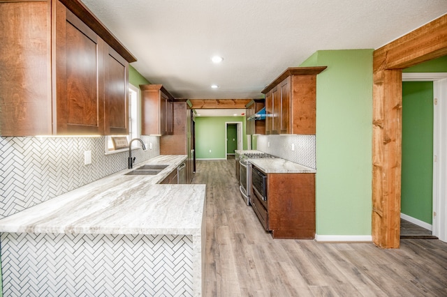 kitchen with decorative backsplash, light stone counters, light hardwood / wood-style floors, sink, and stainless steel stove