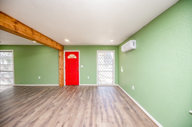 unfurnished room featuring beamed ceiling, a wall mounted air conditioner, and light wood-type flooring