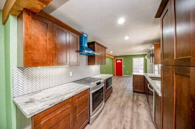 kitchen with light stone countertops, wall chimney exhaust hood, stainless steel appliances, light hardwood / wood-style floors, and decorative backsplash