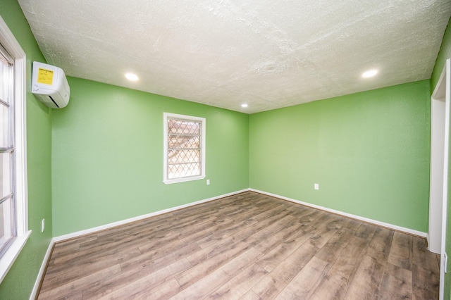 empty room featuring a wall mounted air conditioner, a textured ceiling, and hardwood / wood-style flooring