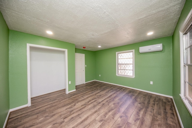 unfurnished bedroom featuring wood-type flooring, a textured ceiling, and a wall mounted AC