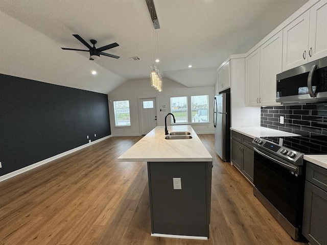 kitchen with pendant lighting, an island with sink, sink, appliances with stainless steel finishes, and vaulted ceiling