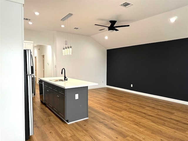 kitchen with appliances with stainless steel finishes, hanging light fixtures, light hardwood / wood-style floors, and a kitchen island with sink