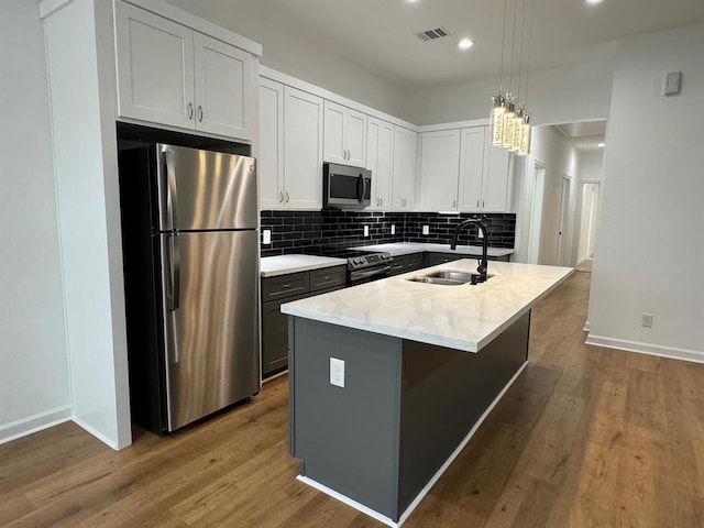 kitchen with an island with sink, sink, pendant lighting, white cabinetry, and appliances with stainless steel finishes