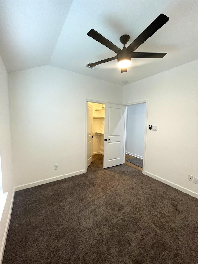 unfurnished bedroom featuring a walk in closet, ceiling fan, a closet, vaulted ceiling, and dark carpet