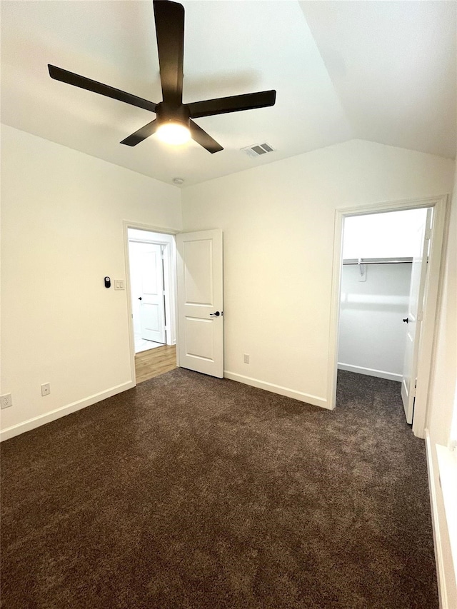 unfurnished bedroom with ceiling fan, a closet, vaulted ceiling, and dark carpet