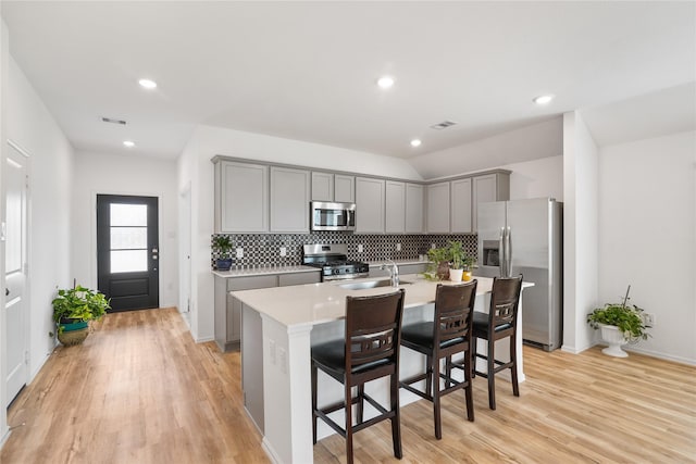 kitchen with a kitchen island with sink, gray cabinets, stainless steel appliances, light countertops, and a kitchen bar