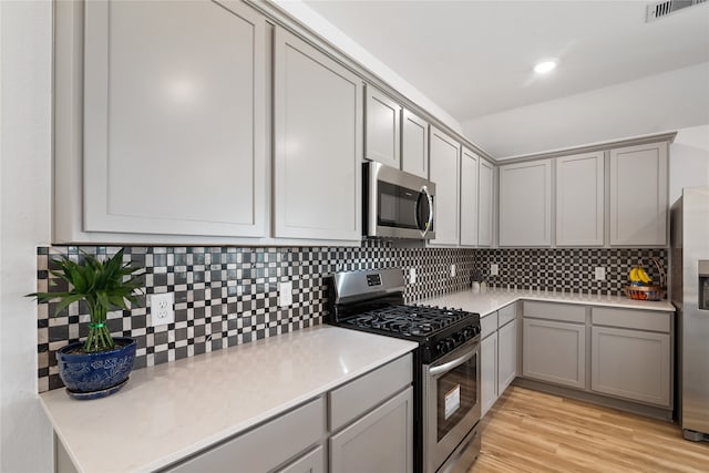 kitchen featuring stainless steel appliances, backsplash, light hardwood / wood-style flooring, and gray cabinetry