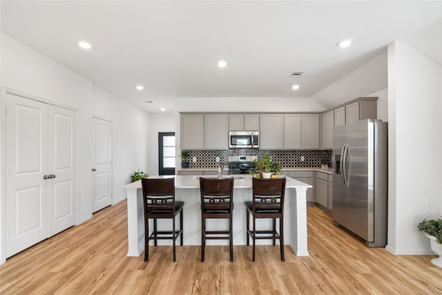 kitchen with gray cabinets, light hardwood / wood-style flooring, a breakfast bar, a center island with sink, and stainless steel appliances