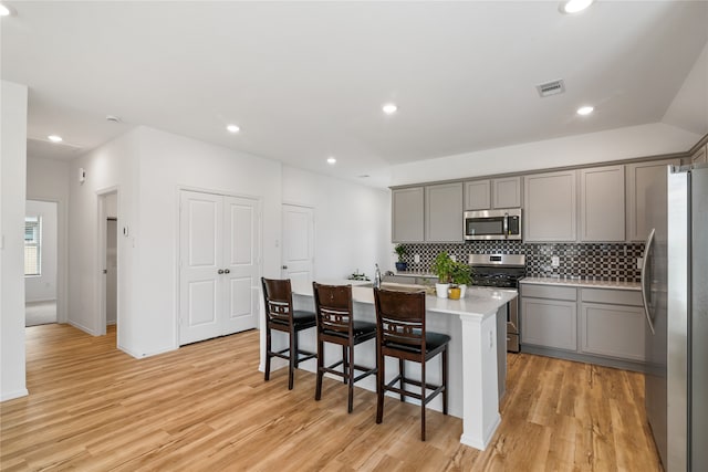 kitchen with a center island with sink, backsplash, light hardwood / wood-style flooring, appliances with stainless steel finishes, and a kitchen breakfast bar