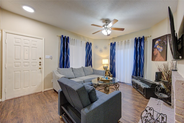 living room with a textured ceiling, ceiling fan, and dark wood-type flooring