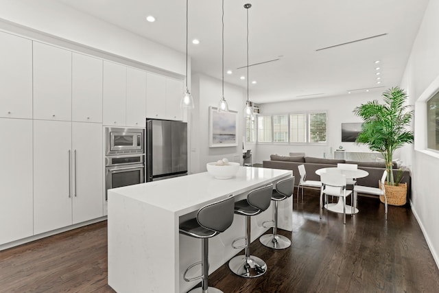 kitchen featuring a kitchen bar, appliances with stainless steel finishes, pendant lighting, white cabinets, and a center island