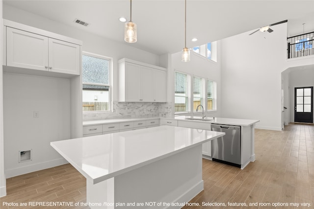 kitchen featuring a kitchen island, ceiling fan, stainless steel dishwasher, white cabinetry, and decorative light fixtures