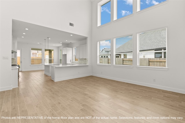 unfurnished living room featuring light hardwood / wood-style floors, a high ceiling, and sink