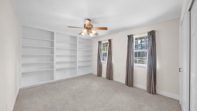 spare room featuring light carpet, crown molding, ceiling fan, and built in shelves