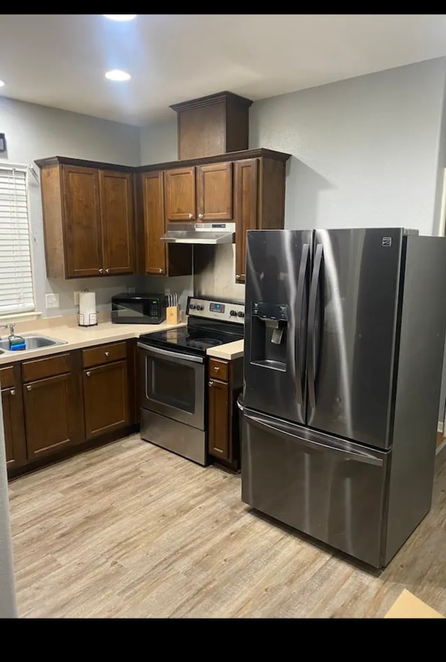 kitchen featuring stainless steel appliances, dark brown cabinetry, sink, and light wood-type flooring