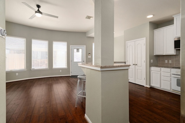 kitchen featuring tasteful backsplash, dark hardwood / wood-style flooring, white cabinetry, a breakfast bar area, and white oven