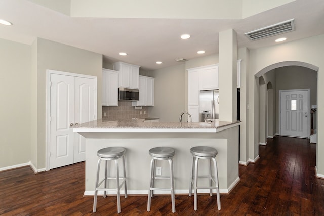 kitchen with a kitchen bar, white cabinetry, stainless steel appliances, and dark hardwood / wood-style flooring