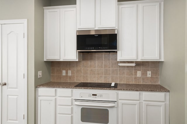 kitchen featuring black electric cooktop, tasteful backsplash, white cabinets, dark stone counters, and white oven