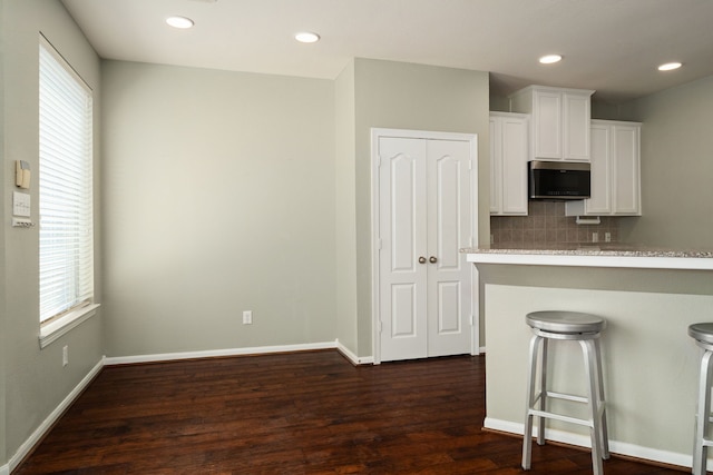 kitchen with decorative backsplash, a breakfast bar, dark wood-type flooring, kitchen peninsula, and white cabinetry