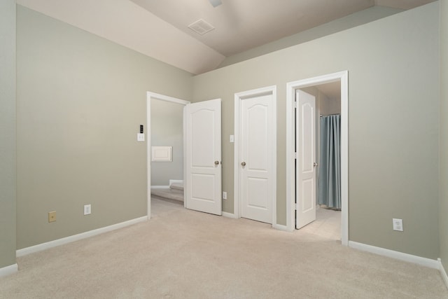 unfurnished bedroom featuring lofted ceiling, light carpet, and ensuite bath