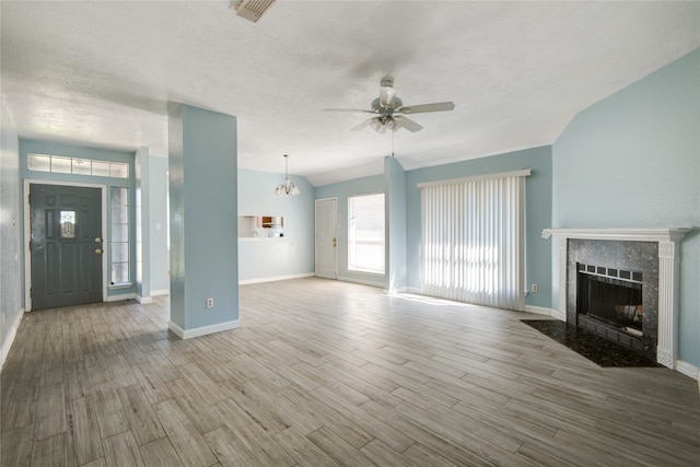 unfurnished living room featuring a fireplace, ceiling fan with notable chandelier, light hardwood / wood-style flooring, and a textured ceiling