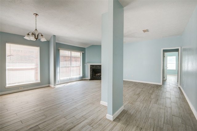 unfurnished living room featuring an inviting chandelier, lofted ceiling, light hardwood / wood-style floors, and a textured ceiling