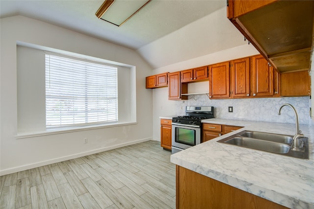 kitchen featuring light wood-type flooring, stainless steel range with gas stovetop, vaulted ceiling, and sink