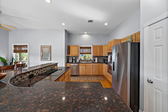 kitchen with decorative backsplash, stainless steel appliances, sink, kitchen peninsula, and light hardwood / wood-style flooring