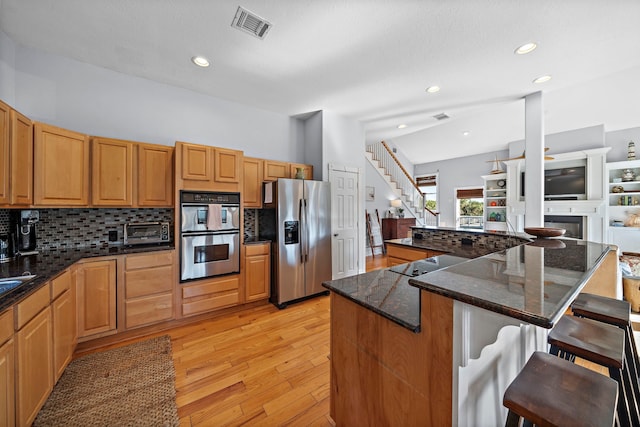 kitchen with a kitchen island, light wood-type flooring, tasteful backsplash, a breakfast bar area, and appliances with stainless steel finishes