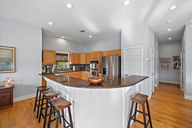 kitchen with light wood-type flooring, a center island, stainless steel appliances, dark stone counters, and a breakfast bar area