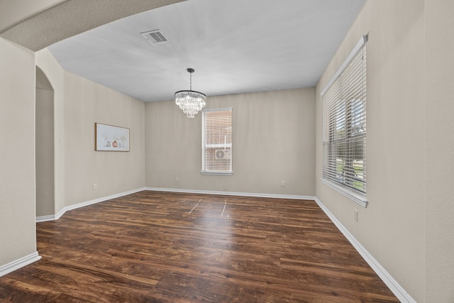 empty room featuring a notable chandelier and dark wood-type flooring