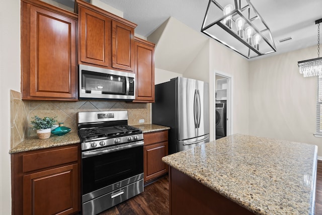 kitchen featuring tasteful backsplash, decorative light fixtures, dark wood-type flooring, appliances with stainless steel finishes, and light stone countertops