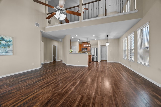 unfurnished living room featuring ceiling fan, dark hardwood / wood-style floors, and a high ceiling