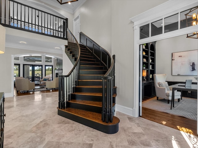 staircase with wood-type flooring, a towering ceiling, french doors, and ornamental molding