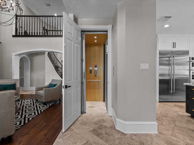 corridor featuring a textured ceiling, light hardwood / wood-style floors, crown molding, and a notable chandelier