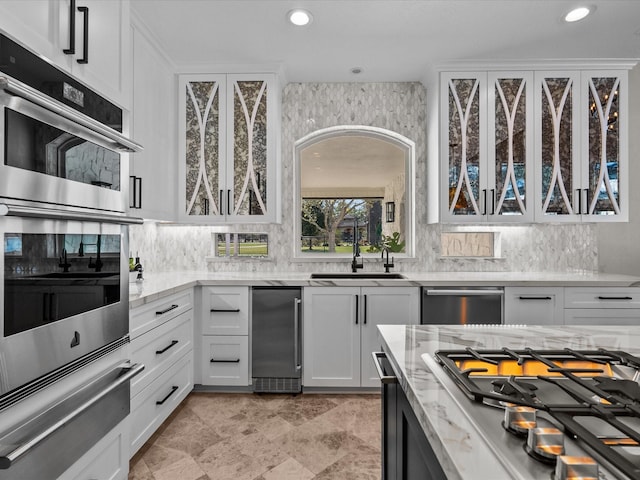 kitchen with decorative backsplash, light stone countertops, stainless steel appliances, sink, and white cabinets