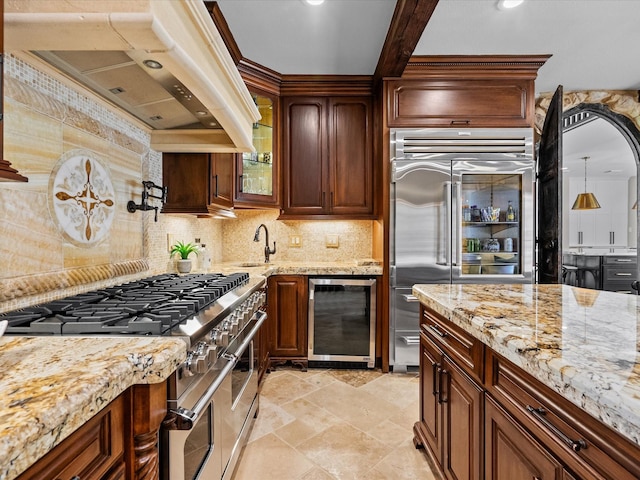 kitchen featuring premium appliances, wine cooler, light stone counters, range hood, and decorative backsplash