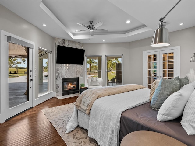 bedroom with dark hardwood / wood-style floors, a tray ceiling, access to outside, and multiple windows