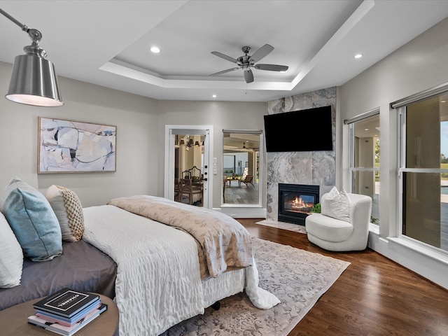 bedroom with a raised ceiling, multiple windows, dark wood-type flooring, and ceiling fan