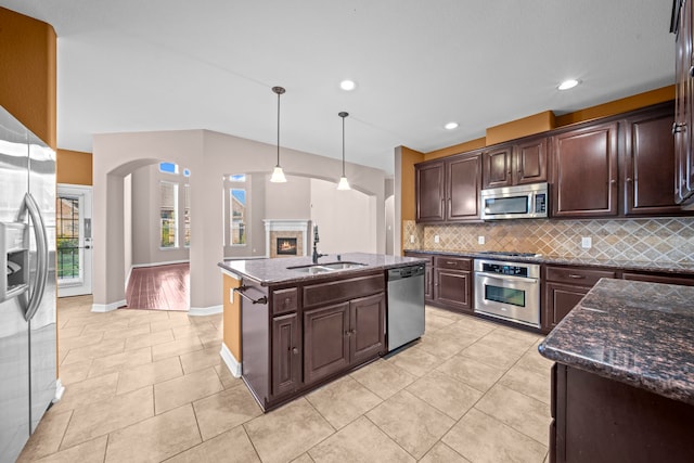 kitchen with appliances with stainless steel finishes, sink, dark brown cabinetry, pendant lighting, and a kitchen island with sink