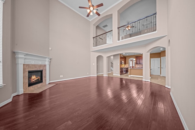 unfurnished living room with ornamental molding, a tiled fireplace, high vaulted ceiling, and wood-type flooring